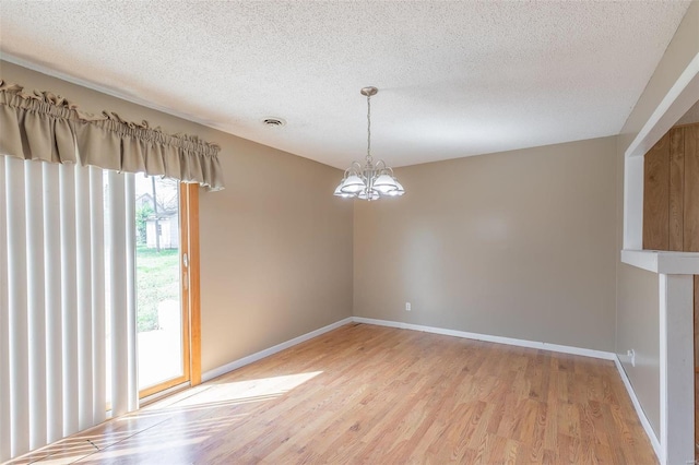 spare room with a textured ceiling, a notable chandelier, and light wood-type flooring