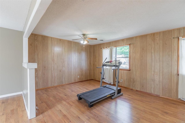 workout room featuring light hardwood / wood-style floors, ceiling fan, wood walls, and a textured ceiling