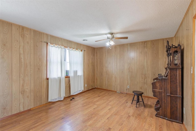 unfurnished room featuring wooden walls, light hardwood / wood-style floors, ceiling fan, and a textured ceiling