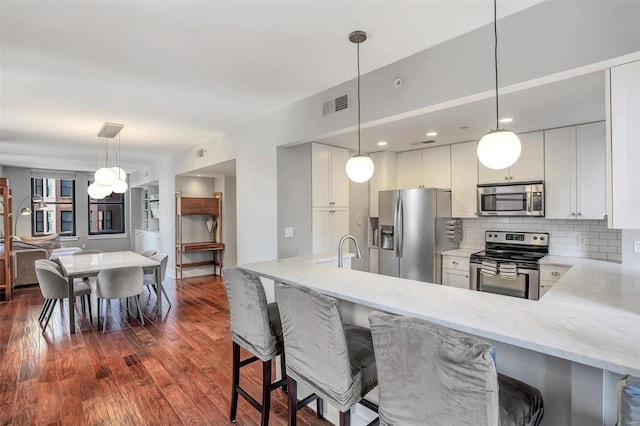 kitchen with pendant lighting, stainless steel appliances, kitchen peninsula, white cabinetry, and dark hardwood / wood-style floors