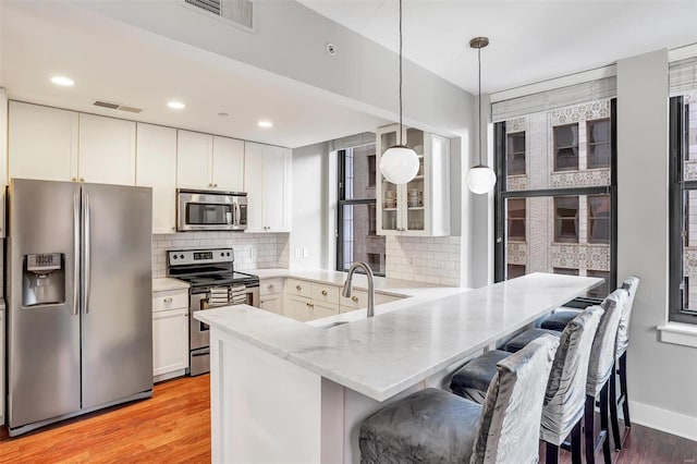 kitchen featuring appliances with stainless steel finishes, pendant lighting, white cabinetry, and light hardwood / wood-style floors