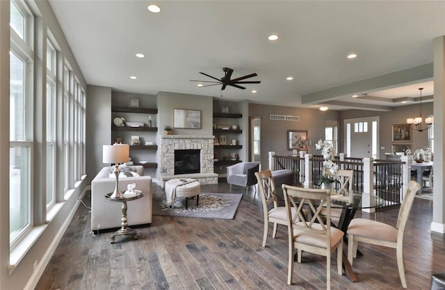 dining area featuring a raised ceiling, a fireplace, dark wood-type flooring, and ceiling fan with notable chandelier