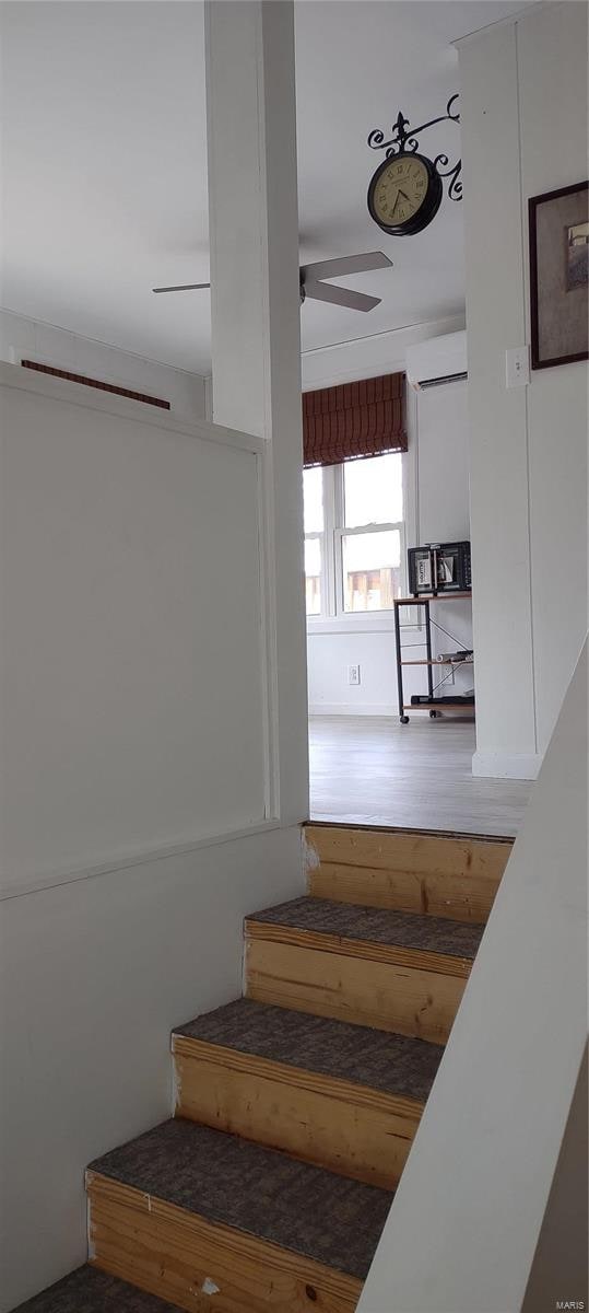 staircase featuring an AC wall unit, ceiling fan, and hardwood / wood-style flooring