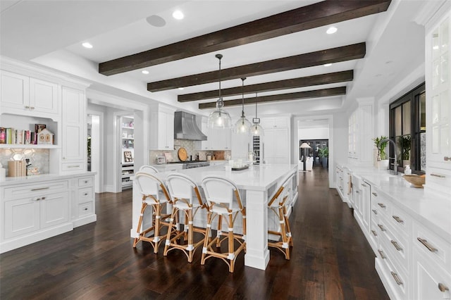 kitchen featuring dark hardwood / wood-style floors, decorative light fixtures, wall chimney exhaust hood, backsplash, and white cabinetry