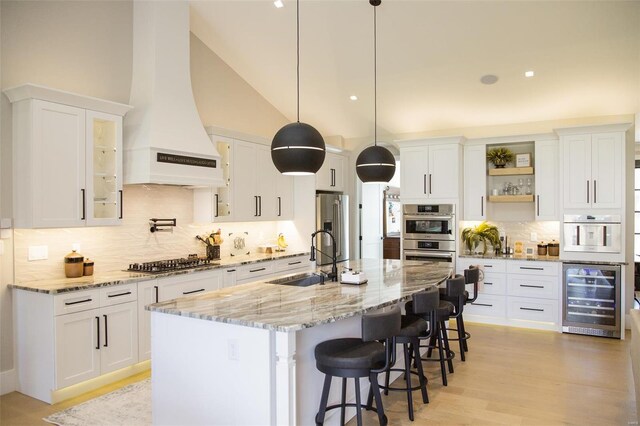 kitchen featuring pendant lighting, custom range hood, appliances with stainless steel finishes, white cabinetry, and beverage cooler