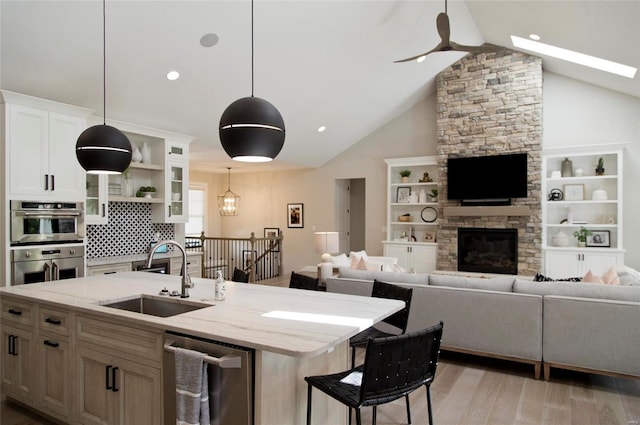 kitchen with decorative light fixtures, sink, white cabinets, a kitchen island with sink, and light stone countertops