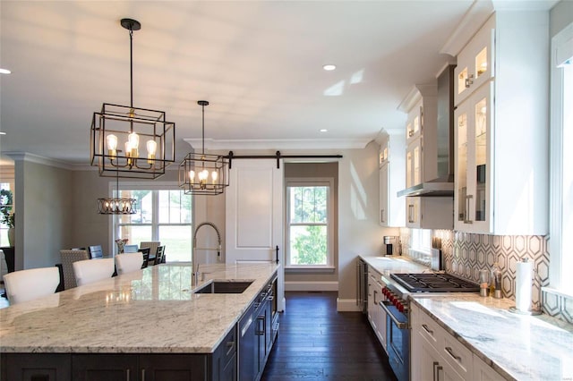 kitchen with sink, white cabinets, high end stainless steel range oven, a center island with sink, and wall chimney exhaust hood