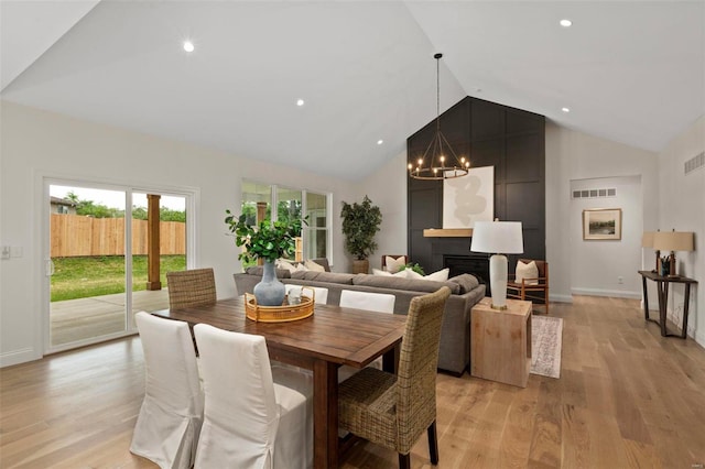 dining area featuring a large fireplace, light hardwood / wood-style floors, vaulted ceiling, and a notable chandelier