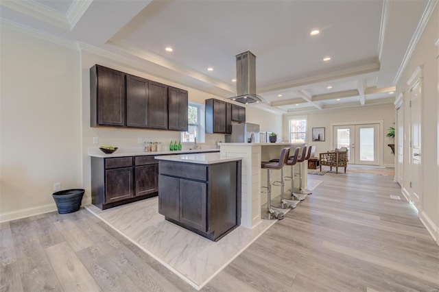 kitchen featuring an island with sink, coffered ceiling, and light hardwood / wood-style flooring