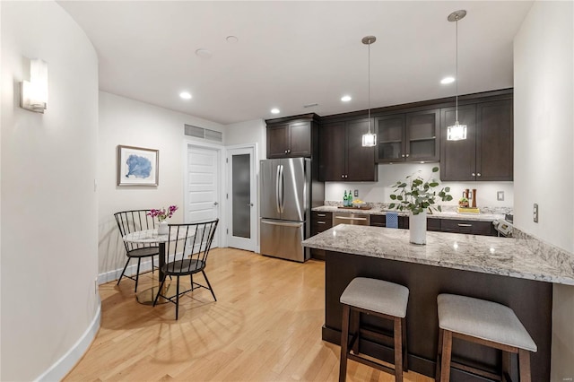 kitchen featuring hanging light fixtures, kitchen peninsula, dark brown cabinets, appliances with stainless steel finishes, and light wood-type flooring