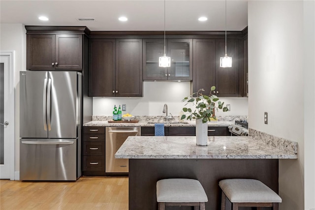 kitchen featuring a breakfast bar, light hardwood / wood-style floors, light stone counters, kitchen peninsula, and stainless steel appliances