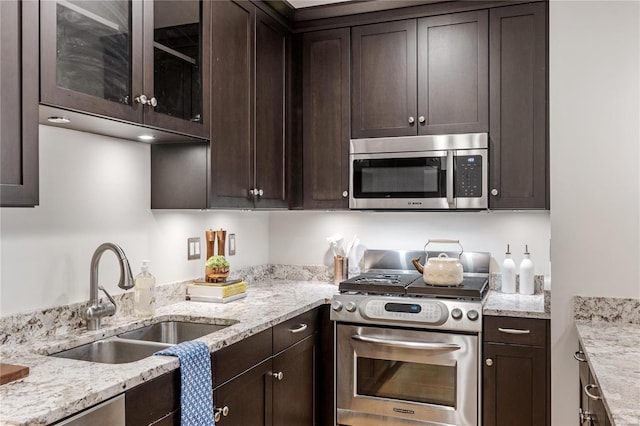 kitchen with light stone countertops, dark brown cabinetry, sink, and appliances with stainless steel finishes