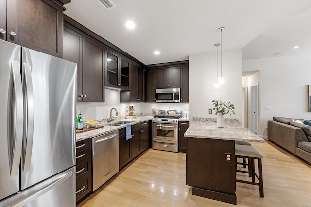 kitchen with appliances with stainless steel finishes, light wood-type flooring, a breakfast bar, dark brown cabinetry, and sink