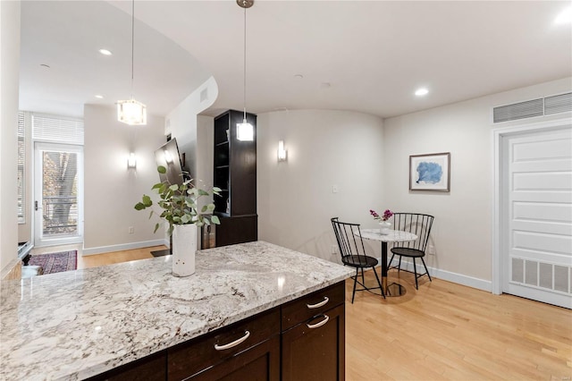 kitchen with pendant lighting, light hardwood / wood-style floors, light stone counters, and dark brown cabinetry