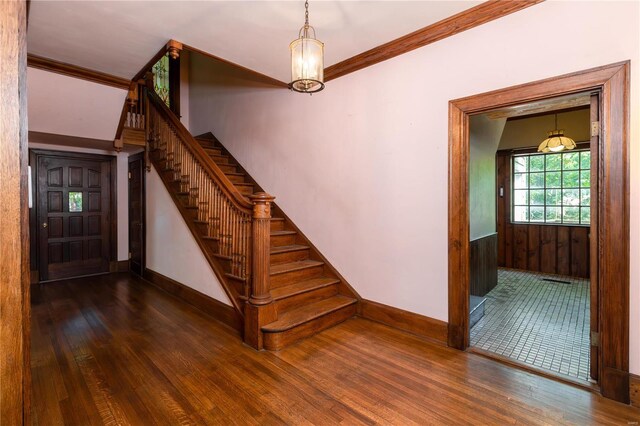 stairs featuring crown molding, wood-type flooring, and an inviting chandelier