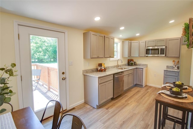 kitchen with gray cabinetry, sink, vaulted ceiling, appliances with stainless steel finishes, and light hardwood / wood-style floors