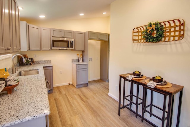 kitchen with lofted ceiling, sink, gray cabinets, light hardwood / wood-style floors, and light stone counters