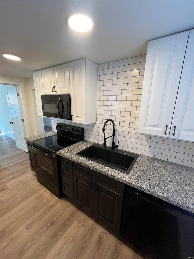 kitchen featuring sink, light hardwood / wood-style floors, backsplash, white cabinetry, and black appliances