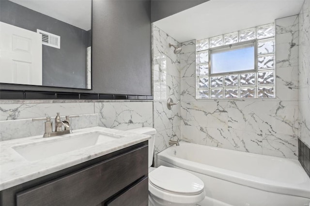 full bathroom with tile walls, toilet, tiled shower / bath, and vanity