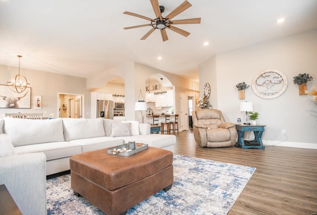 living area featuring arched walkways, recessed lighting, ceiling fan with notable chandelier, wood finished floors, and baseboards