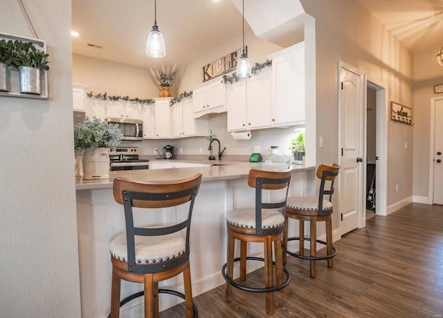 kitchen with appliances with stainless steel finishes, white cabinetry, dark hardwood / wood-style floors, kitchen peninsula, and a breakfast bar