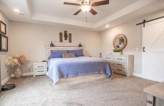 bedroom featuring a barn door, a tray ceiling, ceiling fan, and light colored carpet