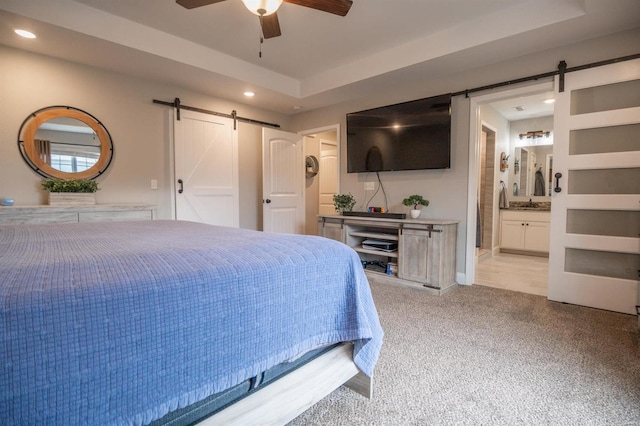 bedroom with ensuite bath, ceiling fan, carpet flooring, a raised ceiling, and a barn door