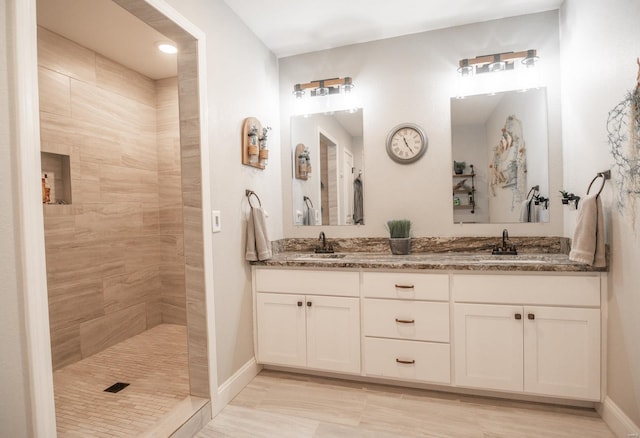 full bathroom featuring a walk in shower, double vanity, a sink, and baseboards