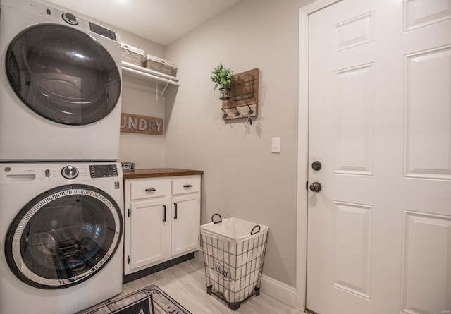 laundry area featuring stacked washer and clothes dryer, light hardwood / wood-style floors, and cabinets