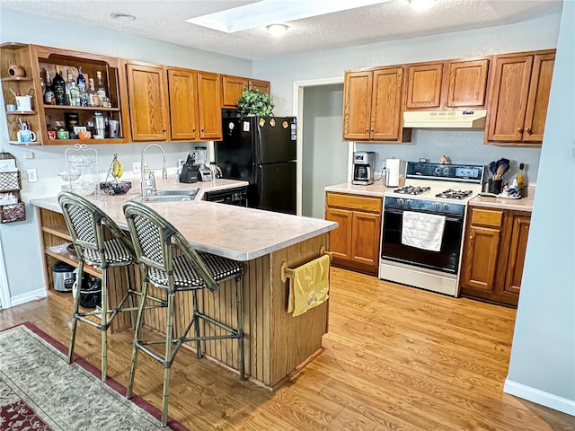 kitchen with a kitchen bar, white gas range oven, sink, black refrigerator, and light hardwood / wood-style floors