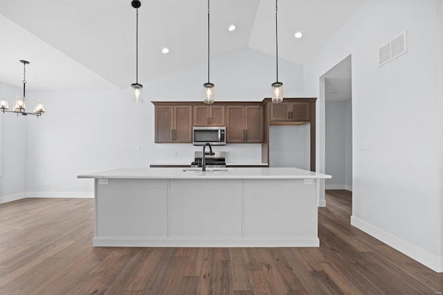 kitchen with appliances with stainless steel finishes, hanging light fixtures, a center island with sink, and dark wood-type flooring