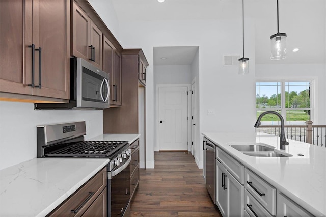 kitchen with appliances with stainless steel finishes, decorative light fixtures, light stone countertops, sink, and dark wood-type flooring