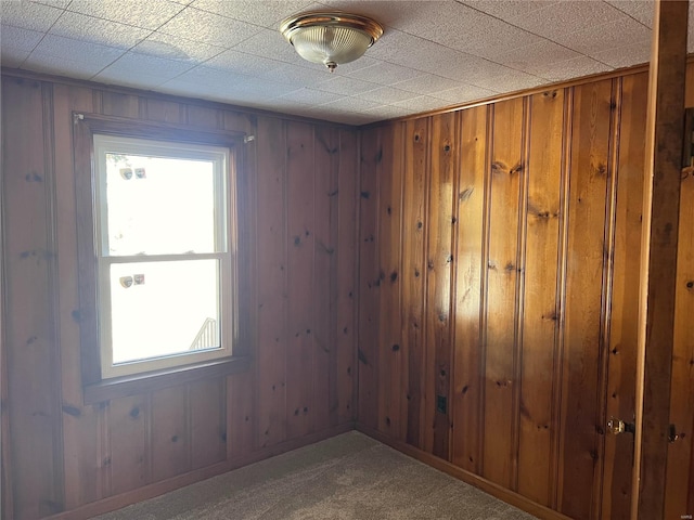 unfurnished room with a wealth of natural light, wooden walls, and dark carpet