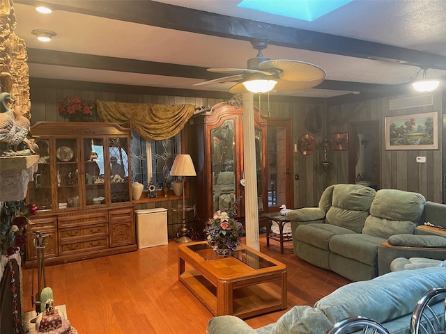 living room featuring ceiling fan, beam ceiling, hardwood / wood-style floors, and a skylight