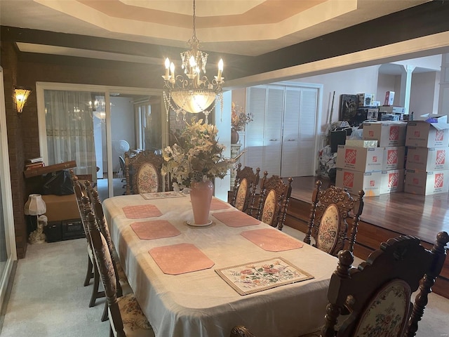 carpeted dining room featuring a tray ceiling, a chandelier, and ornate columns