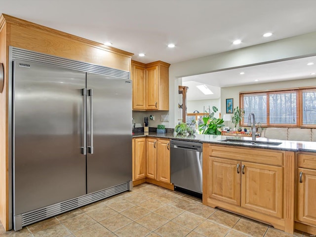 kitchen with stainless steel appliances, sink, light tile patterned floors, and dark stone counters