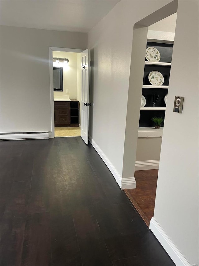 corridor with baseboard heating, built in features, and hardwood / wood-style floors