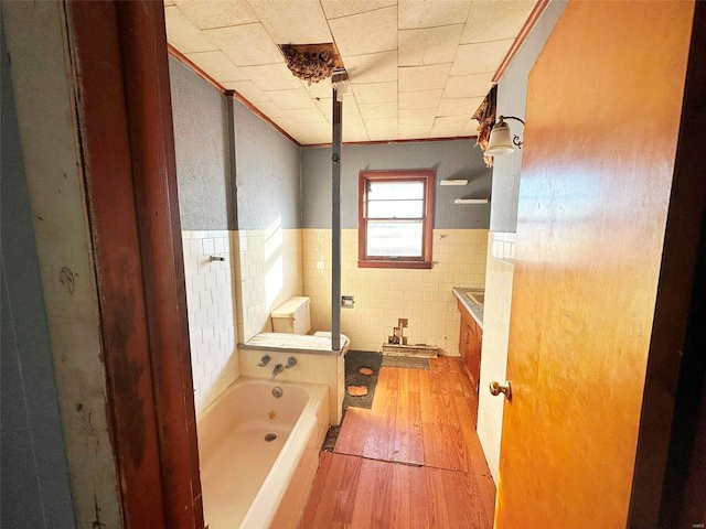 bathroom featuring hardwood / wood-style flooring, crown molding, toilet, tile walls, and a bathing tub