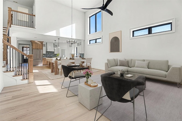 living room with a towering ceiling, ceiling fan with notable chandelier, and light wood-type flooring