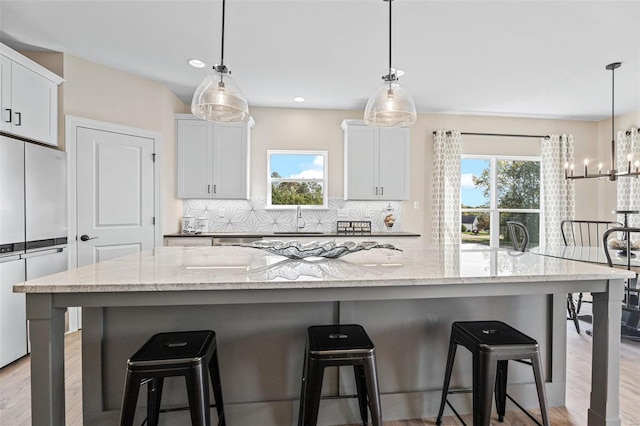 kitchen with backsplash, white cabinets, light stone counters, and stainless steel fridge