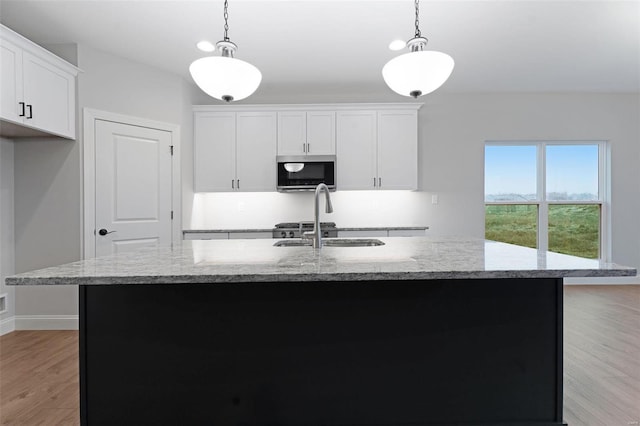 kitchen with a center island with sink, hanging light fixtures, white cabinets, and light wood-type flooring