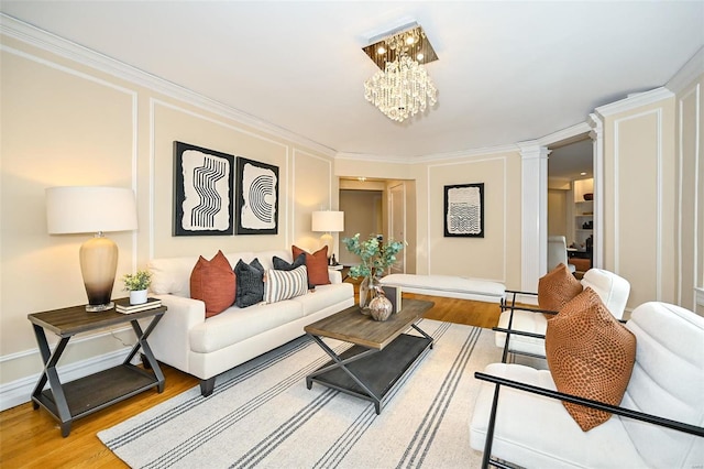 living room featuring decorative columns, hardwood / wood-style flooring, a notable chandelier, and ornamental molding