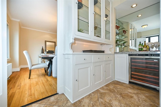 bar with light hardwood / wood-style floors, white cabinetry, beverage cooler, and ornamental molding