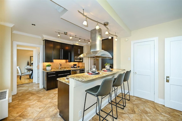 kitchen with sink, crown molding, island range hood, kitchen peninsula, and a breakfast bar area