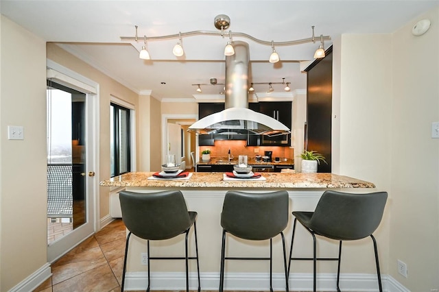 kitchen featuring kitchen peninsula, light stone counters, crown molding, light tile patterned floors, and a breakfast bar area