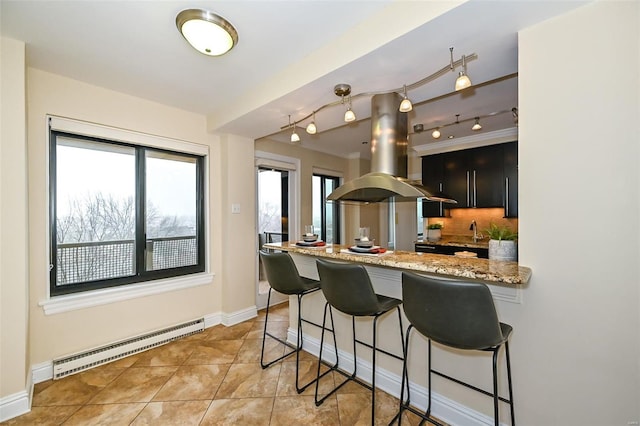 kitchen featuring island exhaust hood, kitchen peninsula, backsplash, light stone counters, and a baseboard radiator