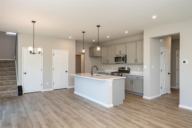 kitchen with stainless steel appliances, light countertops, light wood-style flooring, gray cabinetry, and a kitchen island with sink