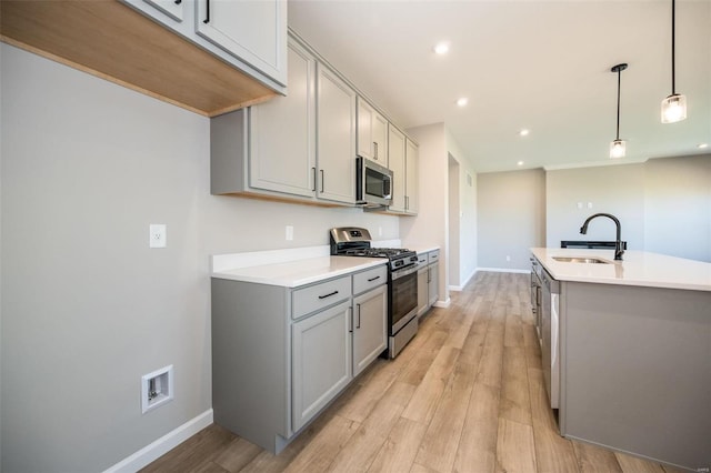 kitchen with decorative light fixtures, light countertops, appliances with stainless steel finishes, a sink, and light wood-type flooring