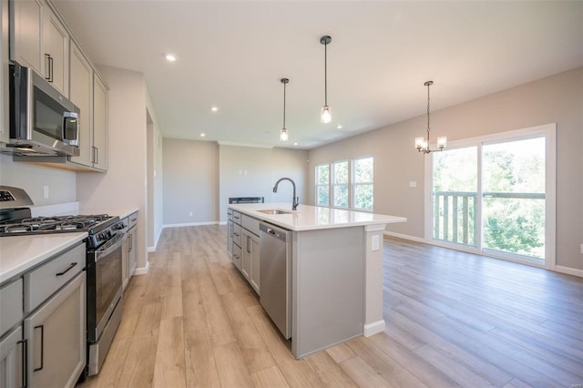 kitchen featuring stainless steel appliances, a kitchen island with sink, gray cabinets, and light countertops