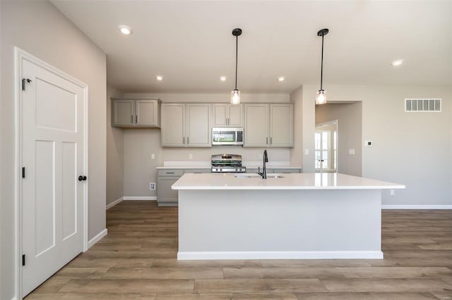 kitchen featuring light countertops, visible vents, gray cabinetry, appliances with stainless steel finishes, and a kitchen island with sink